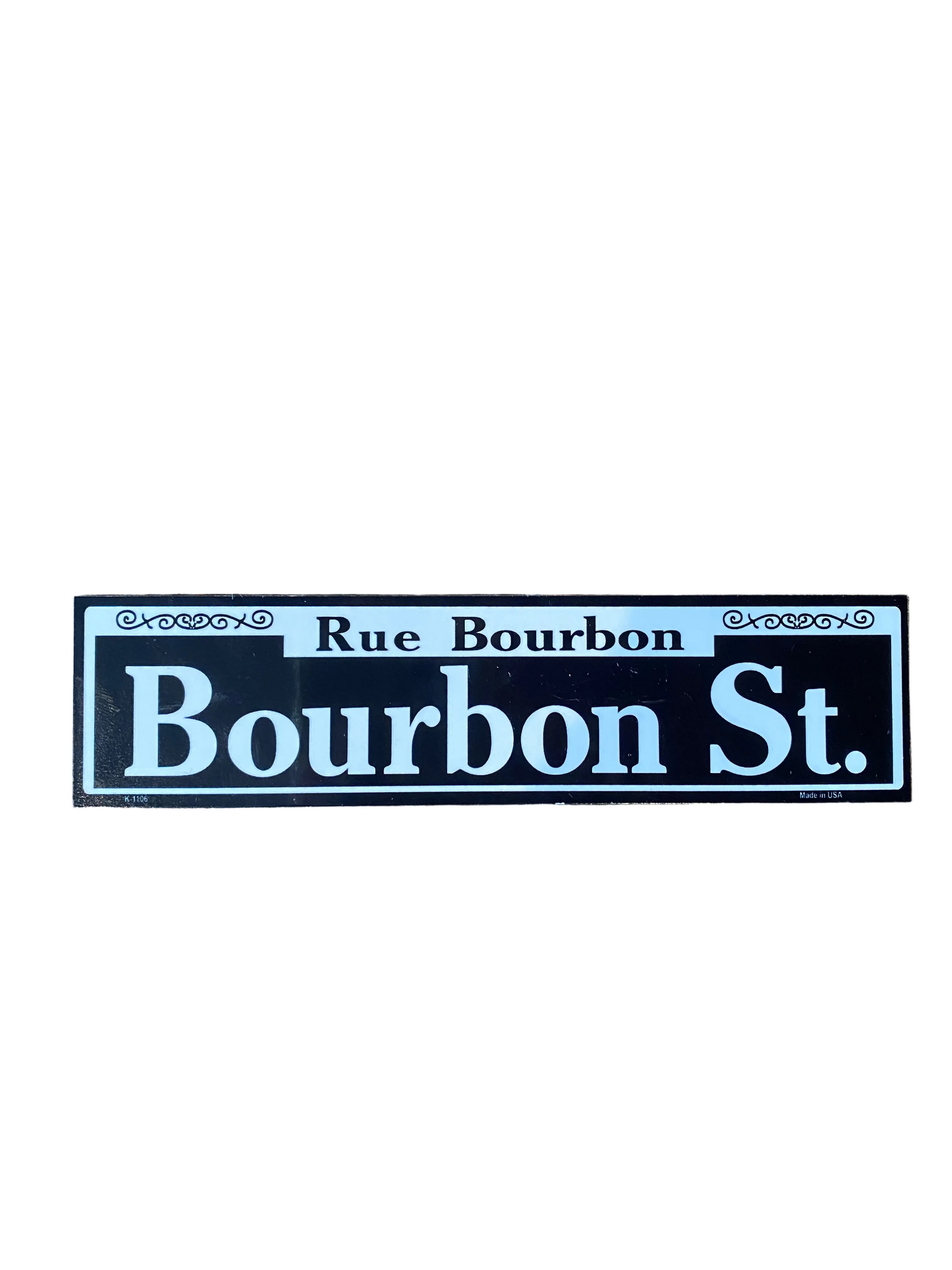 A rectangular street sign reading 'Rue Bourbon Bourbon St.' in white lettering on a black background, placed on a rustic wooden tabletop.